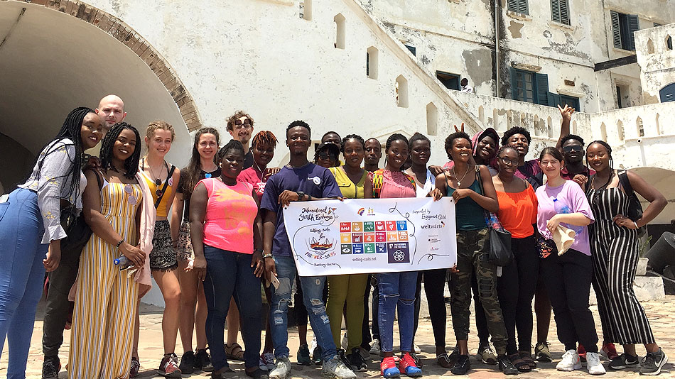 Photo de groupe d'un groupe de jeunes devant un bâtiment ancien. Ils tiennent dans leurs mains une bannière sur laquelle sont inscrits les objectifs de développement durable.