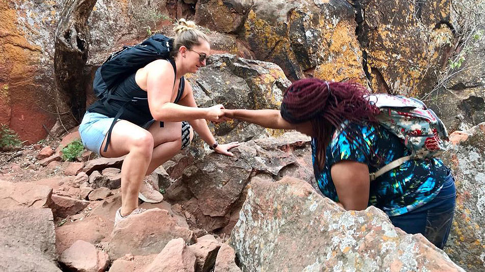 Zwei Teilnehmerinnen überwinden gemeinsam ein Hindernis bei der Wanderung auf den Waterberg.