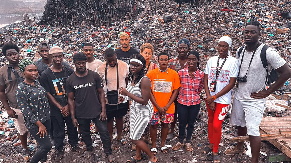 Fünfzehn junge Teilnehmende der Vereine FoGG e.V. und DUNK stehen bei der Fotoaufnahme vor der Müllhalde mit Elektroschrott in Abogblishie in Accra.