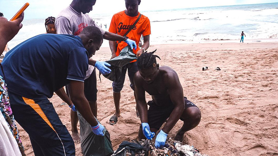 Auf dem Strand von Wakanda in Accra sind sechs junge Teilnehmende der Jugendbegegnung zu sehen, die mit Handschuhen Müll sortieren und in Tüten füllen.