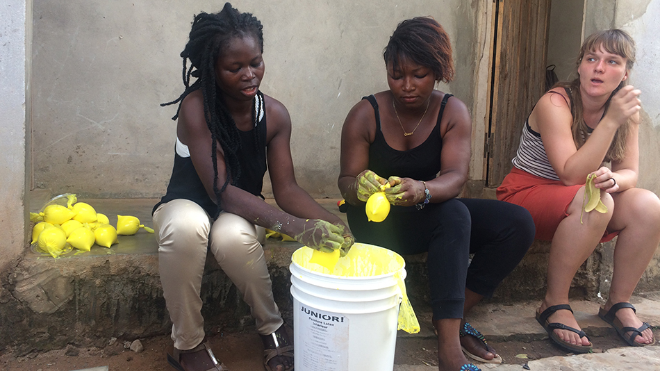 Two participants are sitting on a wall, dyeing props yellow for the play.