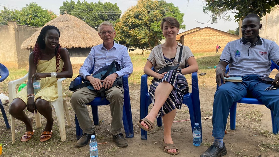 Das Bild zeigt vier Personen, die lächelnd nebeneinander sitzen. Neben ihrem Tandempartner und SES-Experten zeigt das Bild auch ihren ugandischen Austauschpartner Solomon und eine Kollegin.