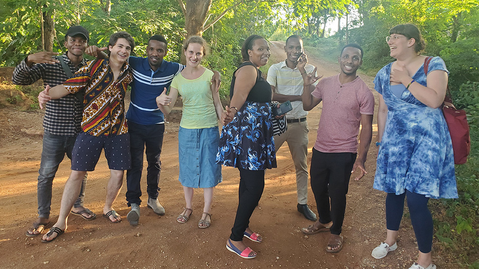 Das Foto zeigt eine Gruppe von acht jungen Menschen auf einem Waldweg. Sie haben teilweise die Arme umeinander gelegt und lachen. Rechts im Bild ist Carolin zu sehen.