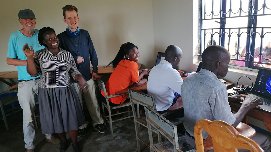 Sur cette photo, on aperçoit trois personnes à gauche : une collaboratrice de l'école primaire, Jonas et Bernd Ziemens, l'expert du SES, sourient à la caméra. À côté d'eux à droite, trois personnes sont assises devant des ordinateurs portables.
