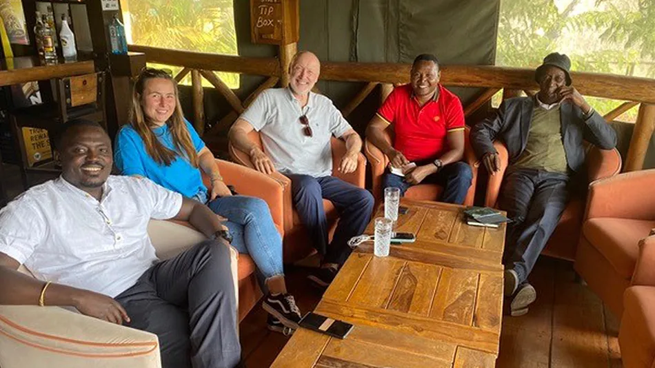 La photo montre Anna et Klaus. Ils/elles sont assi·e·s autour d'une table dans une salle avec trois personnes perçues comme étant des hommes. Toutes ces personnes regardent la caméra et sourient.