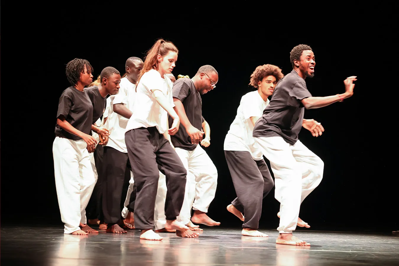 Eine Gruppe junger Menschen wird auf dem Foto bei einer Tanzaufführung gezeigt. Sie tragen schwarze und weiße Kleidung und sind in Bewegung.