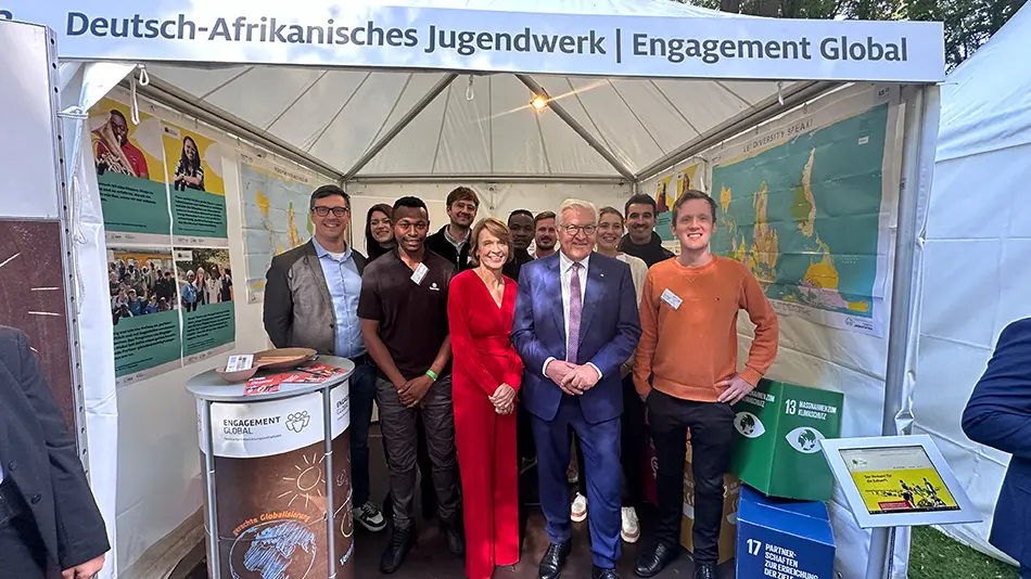 Eine Gruppe von Menschen unter einem weißen Zelt mit der Aufschrift „Deutsch-Afrikanisches Jugendwerk, Engagement Global“. Vorne in der Mitte sind Bundespräsident Frank-Walter Steinmeier und seine Frau Elke Büdenbender. Um sie herum Personen vom DAJW.