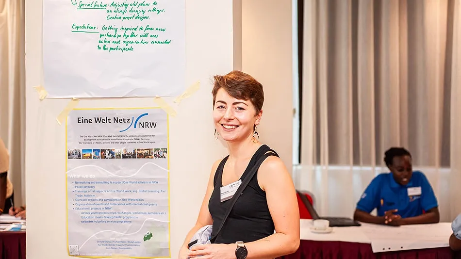 La photo montre la participante Svenja Bloom devant une affiche. Elle sourit au photographe.